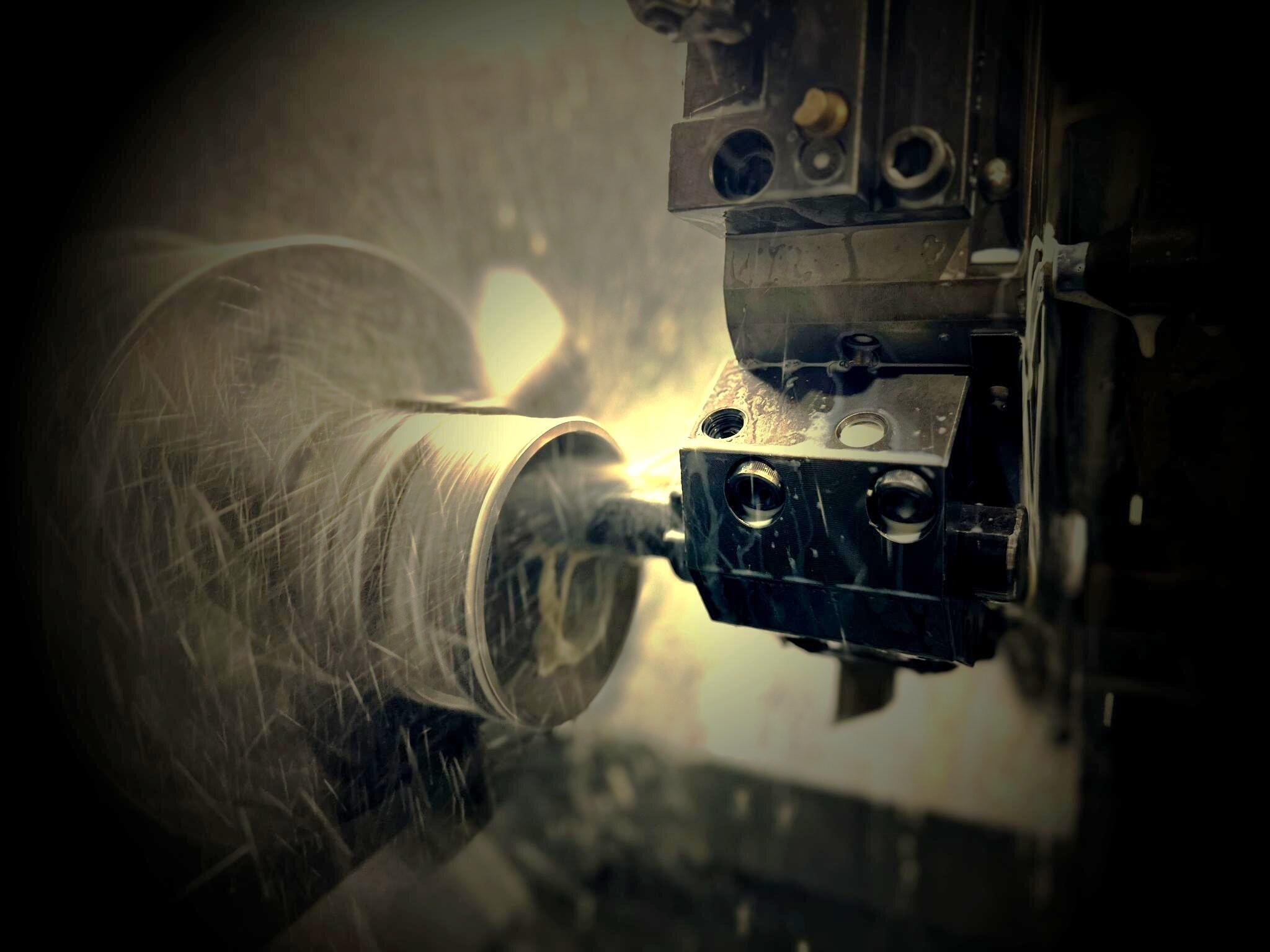 A close-up, high-contrast image of a CNC lathe in the middle of a machining process.