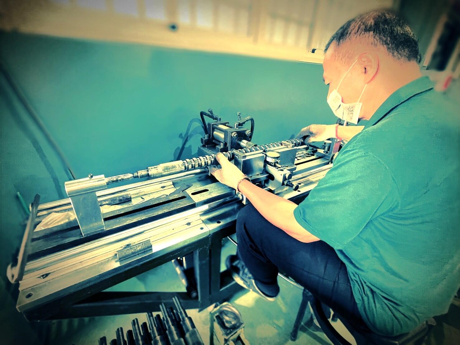 An industrial worker wearing a mask and a green shirt is shown from the side, sitting and operating a machine.